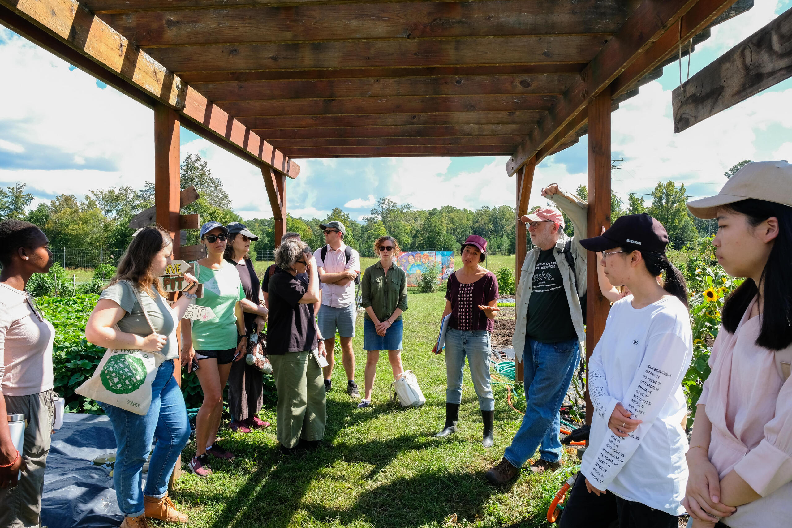 a group of people stand in a group under a shaded area during a visit to a farm